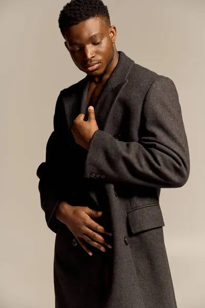 A young handsome African American man poses confidently without a shirt, wearing a stylish coat. He emanates charisma and charm in a minimalist background, expressing elegance and style. — Stock Photo