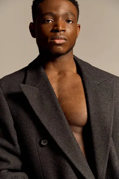A young handsome African American man with a well defined physique poses confidently, wearing a fashionable coat. — Stock Photo