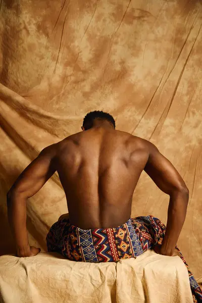 A young handsome African American man showcases his physique in an artistic pose. His strong back and stylish attire contrast beautifully with the textured backdrop, emphasizing confidence and allure. — Stock Photo