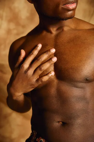 A young handsome African American man poses confidently, showcasing his toned physique against a warm, textured background. His expression reflects self assurance and charisma. — Stock Photo