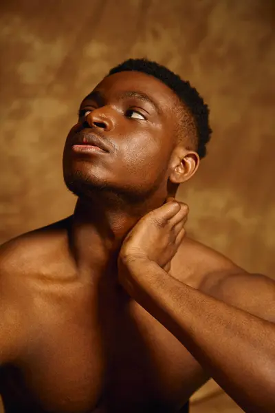 The young man poses topless, showcasing his toned physique against a soft, warm backdrop. His contemplative expression and confident posture create an alluring presence that captivates the viewer. — Stock Photo