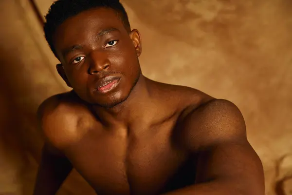 Posing with a strong presence, a young handsome African American man captures attention, revealing his toned physique. The warm tones accentuate his confident demeanor, creating an inviting mood. — Stock Photo