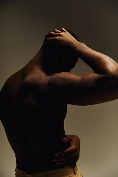 In a striking pose, a young handsome African American man stands topless in creative lighting. His strong physique is highlighted against a neutral backdrop, conveying confidence and artistry. — Stock Photo