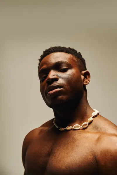 A young handsome African American man poses topless, showcasing a confident expression. His unique necklace adds a touch of charm to the artistic atmosphere, creating an engaging visual moment. — Stock Photo