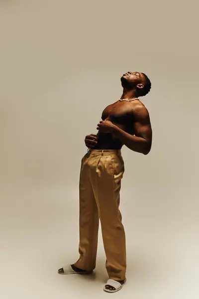 This striking portrait features a young, confident black man posing topless with a relaxed expression. His stylish beige pants complement his athletic build, creating an impressive visual contrast. — Stock Photo