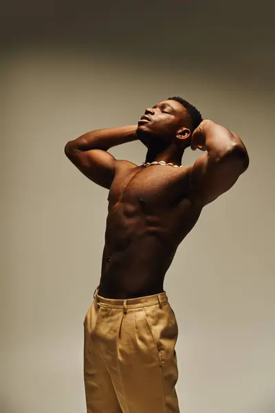 En un estudio elegante, un joven y guapo afroamericano toma una postura segura sin camisa.. - foto de stock