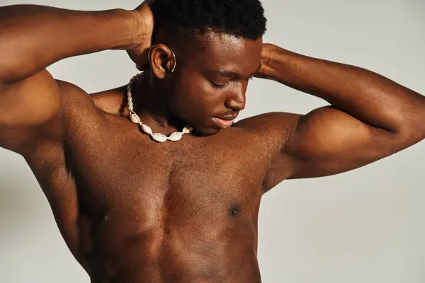 Um jovem afro-americano bonito está marcando uma pose confiante topless, demonstrando sua construção atlética e estilo. Ele está usando um colar distinto que adiciona talento ao seu olhar. — Fotografia de Stock