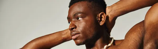 A young African American man poses confidently without a shirt, showcasing his sculpted arms and relaxed demeanor. — Stock Photo