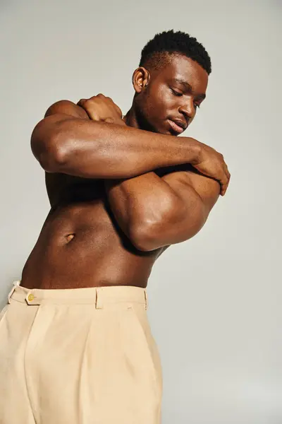 A young handsome African American man poses confidently without a shirt, highlighting his strong physique. He stands against a neutral backdrop, adding an artistic flair to the moment. — Stock Photo