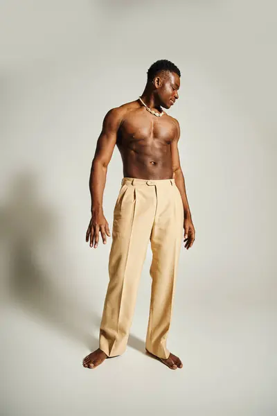 A young attractive African American man stands confidently with a relaxed posture, wearing stylish beige pants and displaying a toned physique. — Stock Photo