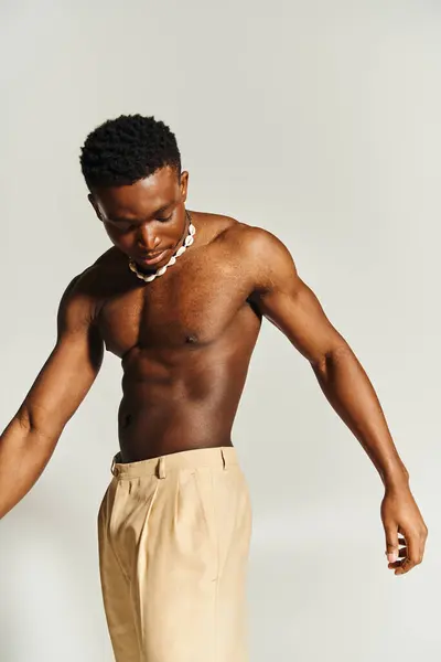 A young and attractive African American man stands in a relaxed posture, showcasing his toned physique. He wears stylish trousers paired with a unique necklace, embracing a self assured expression. — Stock Photo