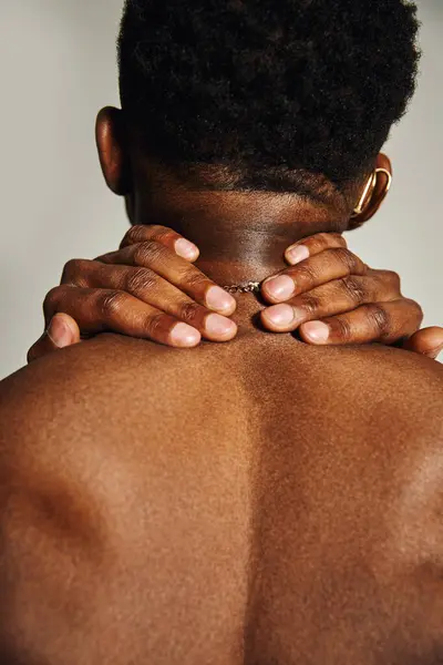 Un giovane uomo afroamericano si alza con fiducia, mostrando il suo fisico tonico. Le sue mani poggiano sul collo, creando un'atmosfera suggestiva e intima. L'illuminazione soffusa migliora l'umore. — Foto stock
