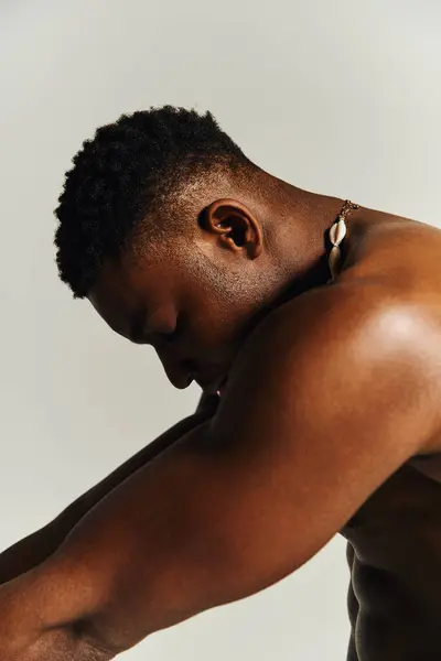 Un jeune homme afro-américain beau pose avec un air de confiance. Son haut du corps est exposé, soulignant les traits musculaires, comme il regarde vers le bas d'une manière réfléchie. — Photo de stock