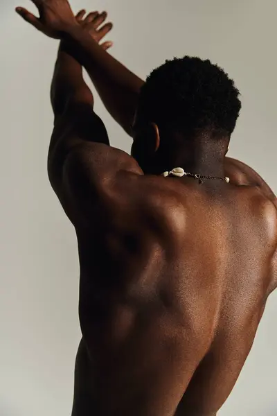 A young, attractive African American man poses topless, highlighting his well defined physique and confidence. The neutral background emphasizes the subjects strong presence and unique style. — Stock Photo