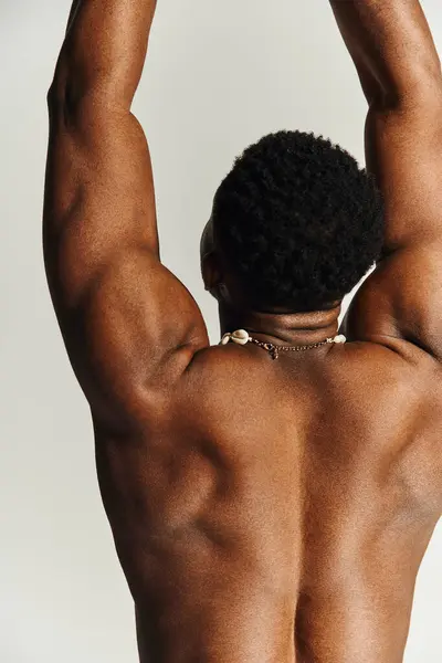 A young African American man displays his impressive physique while posing topless. The background hints at a creative photoshoot vibe highlighting his strength and confidence. — Stock Photo