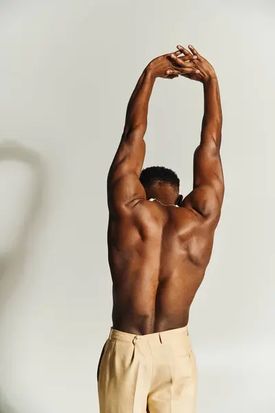 A young, muscular African American man poses topless while stretching his arms above his head. His strong physique is framed against a soft backdrop, showcasing his confidence and style. — Stock Photo