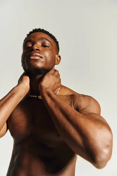 A young, handsome African American man poses confidently while topless, showing off his toned physique. His expression exudes charisma and charm against a minimalistic backdrop. — Stock Photo