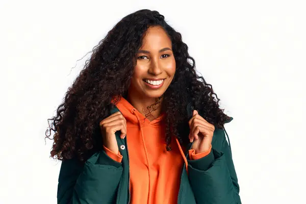 A joyful woman showcases her long curly hair while wearing a trendy outfit in a vibrant setting. — Stock Photo