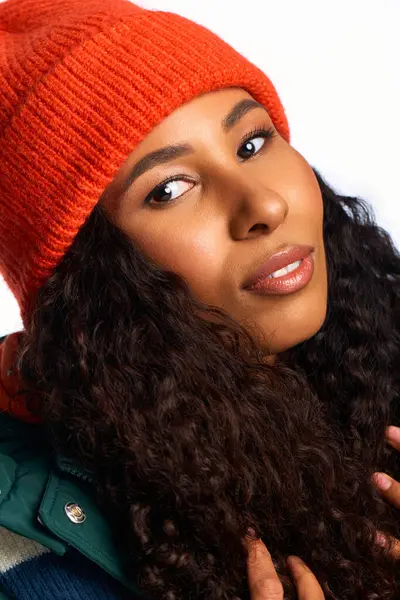 A fascinating woman with curly hair wears an orange beanie and poses confidently in a cozy outfit. — Stock Photo