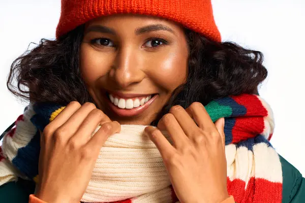 Smiling woman embraces the winter spirit with a colorful scarf and warm beanie, radiating joy. — Foto stock