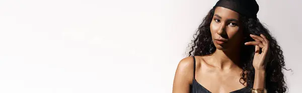 Beautiful woman with curly hair and stylish head wrap exudes confidence in a serene studio setting — Stock Photo