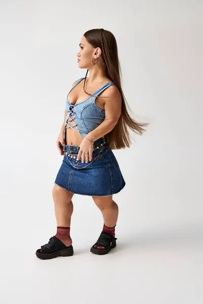 Una mujer joven y elegante con baja estatura modela con confianza la ropa de mezclilla en un estudio moderno. - foto de stock