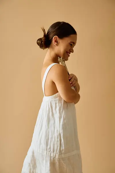 A young woman with short stature gently holds flowers while dressed elegantly in soft lighting. — Stock Photo
