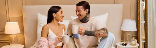 Любящая молодая пара улыбается друг другу за чашкой кофе в красиво оформленной спальне. — стоковое фото