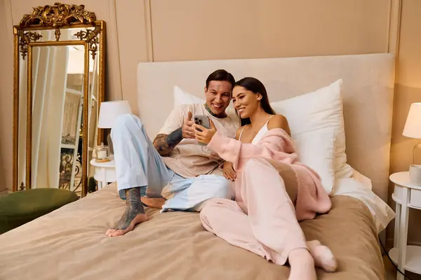 Couple aimant se détend sur un lit, partager des rires comme ils regardent leur téléphone et profiter de l'autre. — Photo de stock