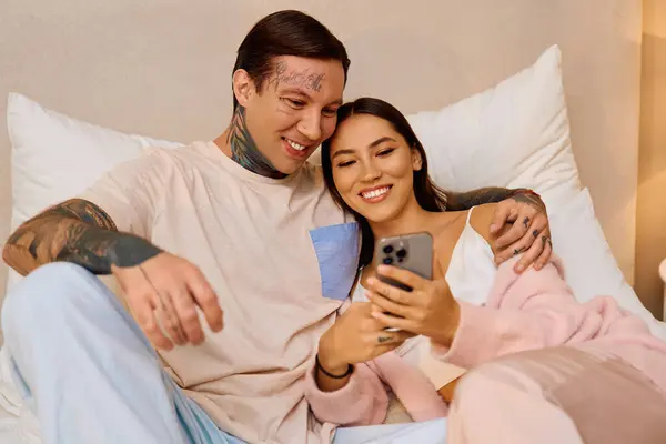 Ein Paar lächelt zusammen und genießt einen gemütlichen Moment, während es auf einen Telefonbildschirm blickt. — Stockfoto