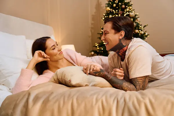 A loving couple laughs and looks into each others eyes while relaxing on their bed. — Stock Photo