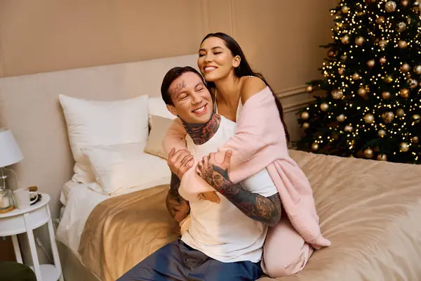 Young couple embraces lovingly, enjoying cozy moments by their decorated Christmas tree. — Stock Photo