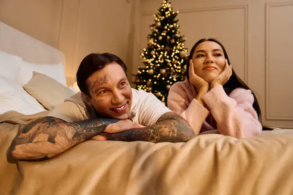 Couple se détend sur un lit, profiter de l'autre compagnie à côté d'un arbre magnifiquement décoré. — Photo de stock