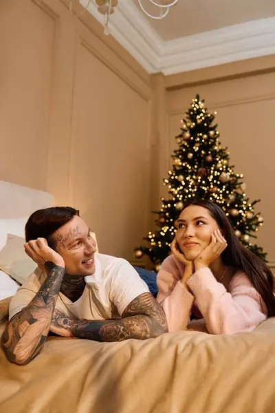 Jeune couple profite d'un moment tendre sur un lit confortable près d'un arbre de vacances joliment décoré — Photo de stock