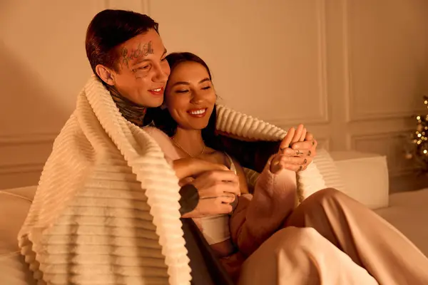 A loving couple snuggles under a blanket, sharing joyful laughter and tender moments at home. — Stock Photo