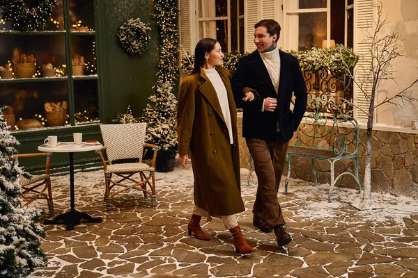 A young couple enjoys a cozy winter evening walk in a charming, snow covered courtyard. — Stock Photo