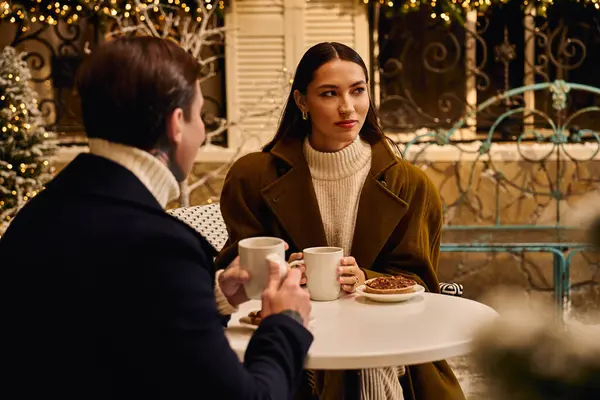 A loving couple shares warm beverages and pastries while seated outside in a festive atmosphere. — Stock Photo