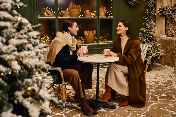 A young couple shares a cozy moment over warm drinks, surrounded by winter decorations and snow. — Stock Photo