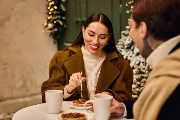 Young couple shares laughter and dessert while savoring warm drinks in a winter atmosphere. — Stock Photo