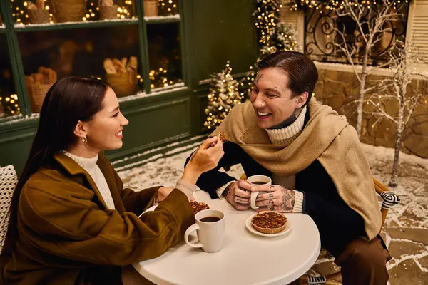 Loving couple enjoys warm drinks and pastries while smiling in a festive winter environment. — Stock Photo