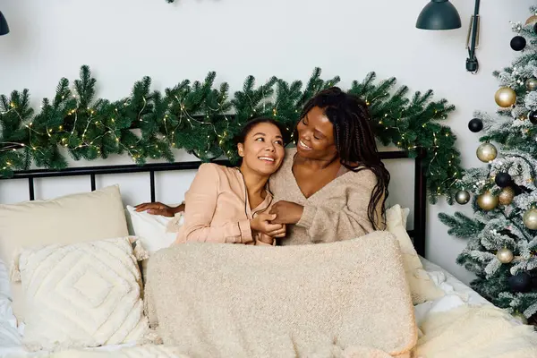 Deux femmes joyeuses partagent un moment tendre sous une couverture confortable dans un cadre festif. — Photo de stock