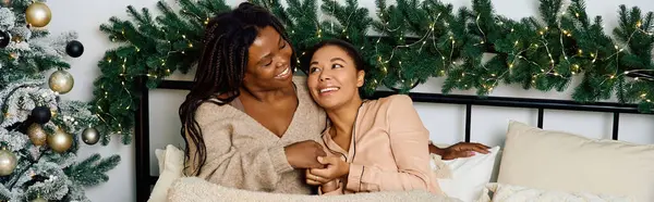 Two joyful women relax in bed, enjoying a cozy winter evening with festive decorations. — Stock Photo
