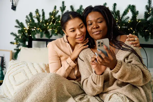 Deux femmes s'assoient ensemble sur un lit, profitant mutuellement de la compagnie tout en regardant un téléphone. — Photo de stock