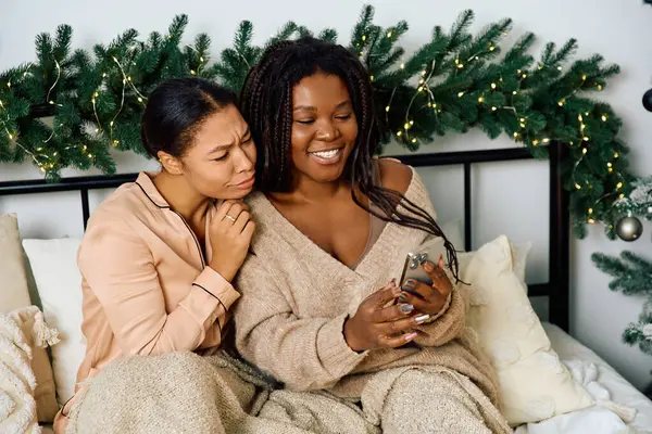 Deux femmes se blottissent ensemble sur un lit, partageant joyeusement leurs souvenirs tout en étant entourées d'un décor de vacances. — Photo de stock