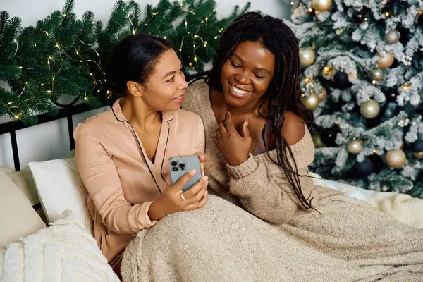 Deux femmes se détendent sur un lit confortable, souriant et appréciant l'esprit de vacances pendant qu'elles sont au téléphone. — Photo de stock