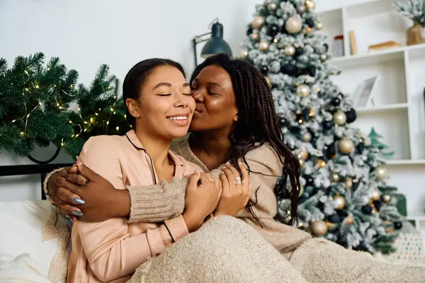 Dos mujeres se abrazan calurosamente en un sofá acogedor, celebrando el amor y la unión durante el invierno. - foto de stock