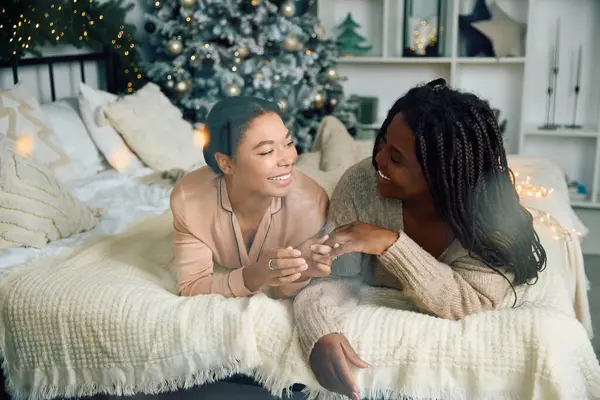 Duas mulheres sorriem e desfrutam uma da outra em uma cama macia cercada por uma decoração festiva. — Fotografia de Stock