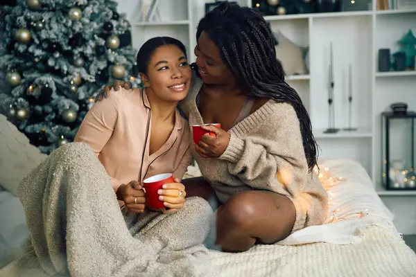 Loving women share warmth and affection while sitting on a cozy bed during the holidays. — стоковое фото