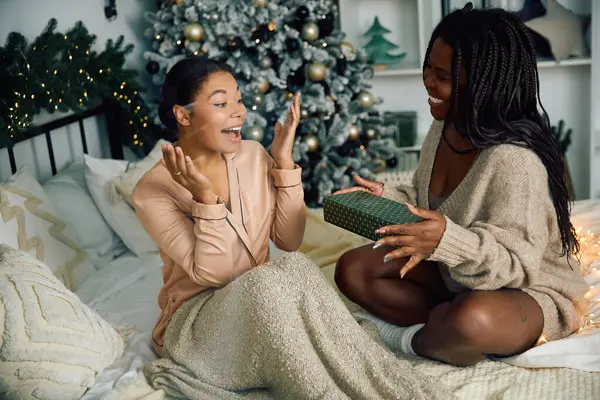 Two women celebrate together, exchanging gifts in a beautifully decorated living space. — Stock Photo