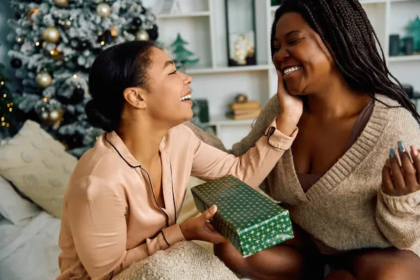 Two women share laughter and warmth while exchanging gifts in a festive holiday setting. — Stock Photo